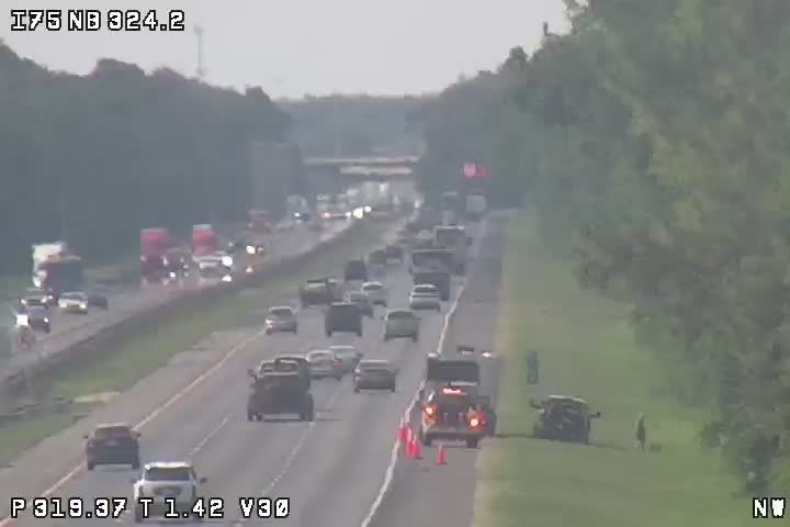Traffic incident with emergency vehicle and cones on-scene personnel on the shoulder.