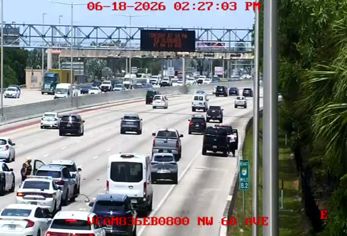 Two people are standing next to a stopped car on the shoulder, possibly a responder scene.