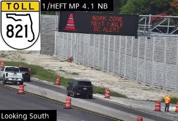 Work zone with personnel and traffic control devices and signage indicating a work zone ahead.