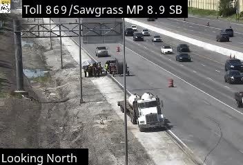 Construction vehicles and workers are present on the shoulder of the highway.
