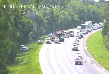 Multiple vehicles stopped in traffic, some appear damaged, smoke visible.
