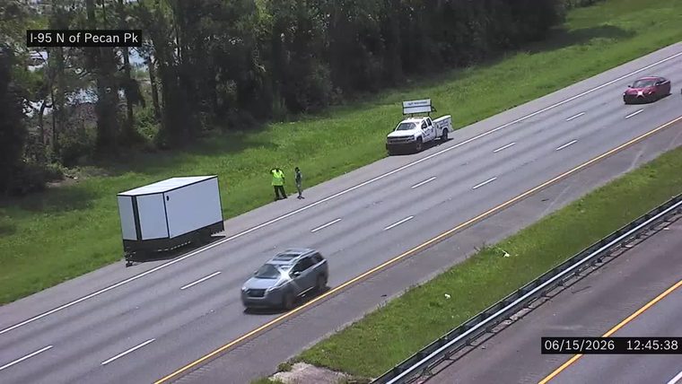 Two people and a truck are on the shoulder of the highway near a trailer.