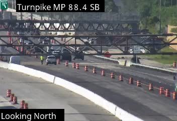 A person in a safety vest is standing near vehicles on the roadway.