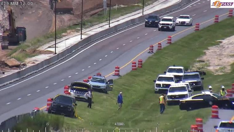 Multiple vehicles and personnel on the shoulder, including a police car.