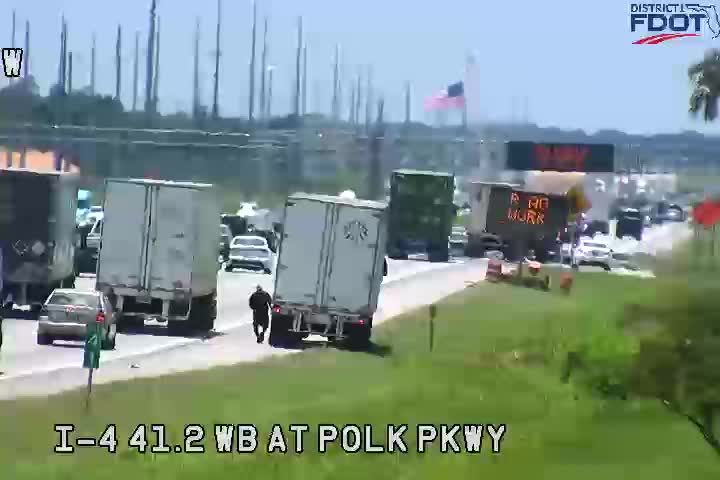 Traffic incident with a person walking near trucks and a "No Work" sign.