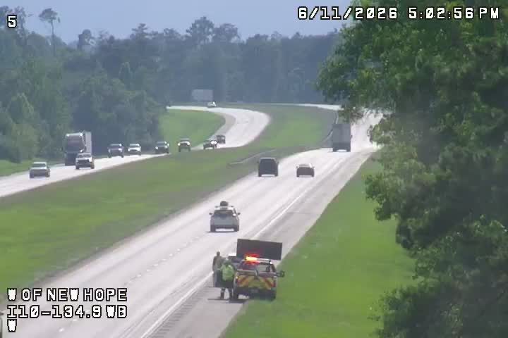 Two people and a vehicle with flashing lights are on the shoulder of the road.