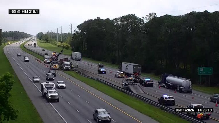 Multiple police cars and tow trucks at a roadside incident on I-95.