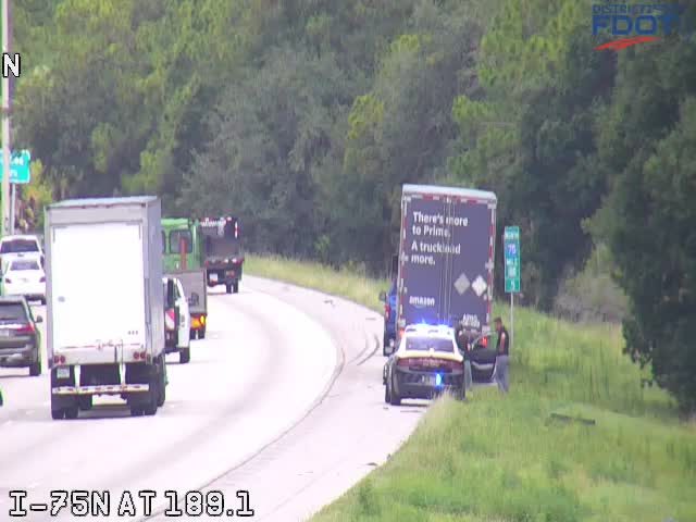 Police car and officers attending to a vehicle on the shoulder of the highway.