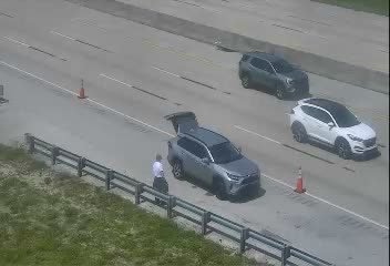 Person in uniform standing by an open car trunk on the side of the road.