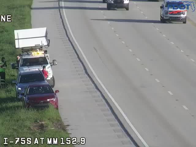 Tow truck and two cars pulled over on the shoulder with personnel present.