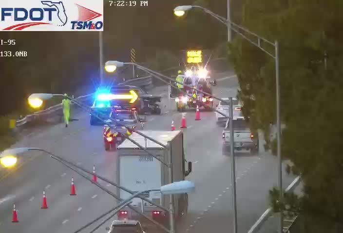 Police car with blue flashing lights and a person in a high-visibility suit on the roadway