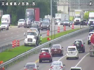 Emergency responder assisting a vehicle on the side of the highway with traffic cones.