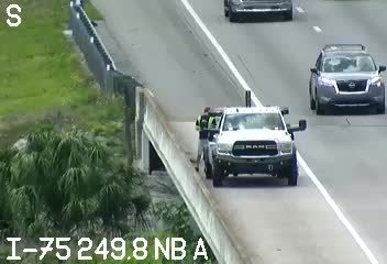 A white pickup truck with a person in the driver's seat is stopped on the shoulder of the highway.