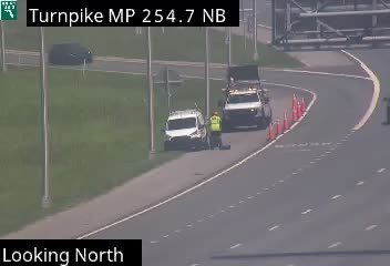 Two workers and a tow truck are on the shoulder with traffic cones.