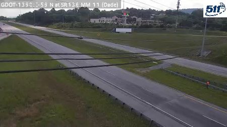 Person in orange vest on shoulder near highway, possibly responding to an incident.