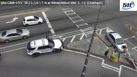 Police car and two workers near a silver sedan on the right side of the roadway