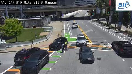 Two individuals in safety vests are attending to a black car on the roadway.