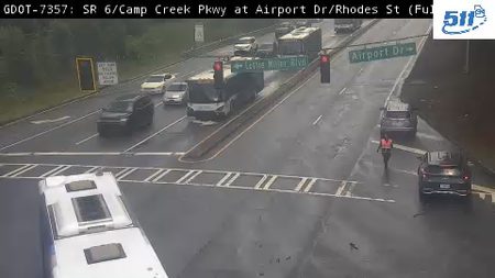 Person in orange vest directing traffic on a wet roadway.
