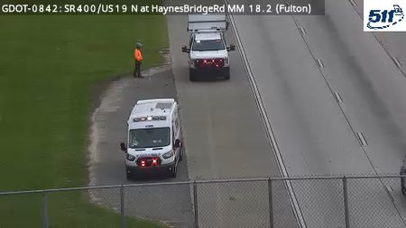 Ambulance and utility truck on the roadside with a person in an orange vest.