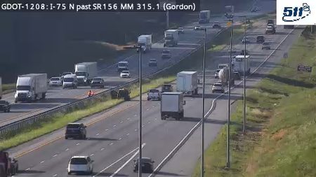 Person in orange vest on highway shoulder near stopped vehicles.