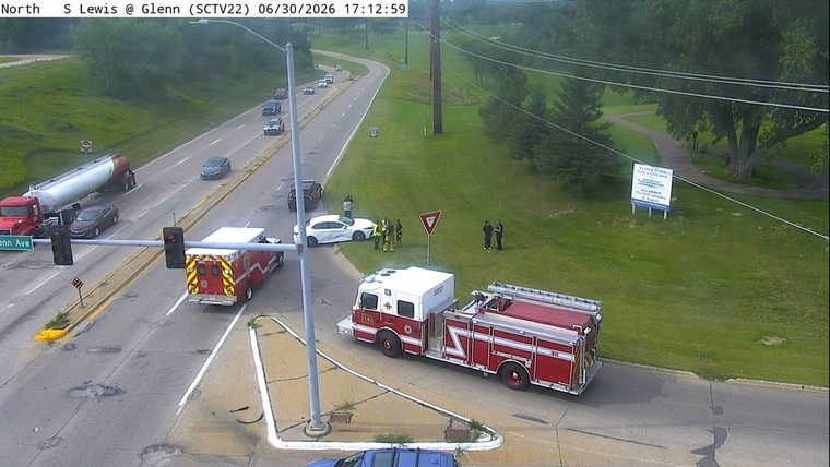 Fire truck and ambulance on the right side of the intersection, with a white car and several people near it.