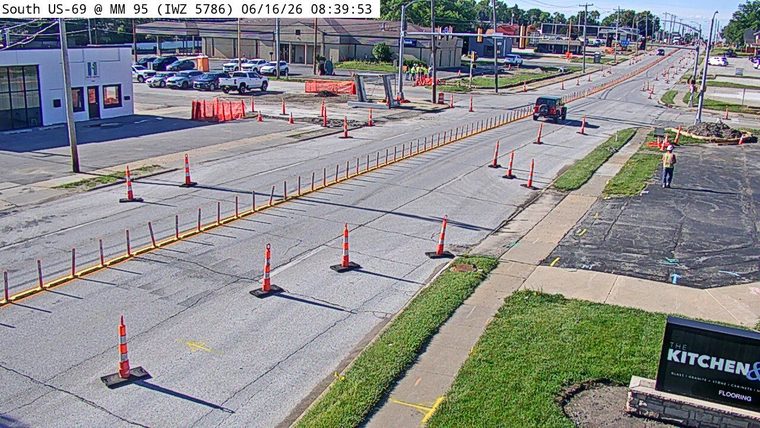 Construction worker present on the roadway with traffic cones and barriers.