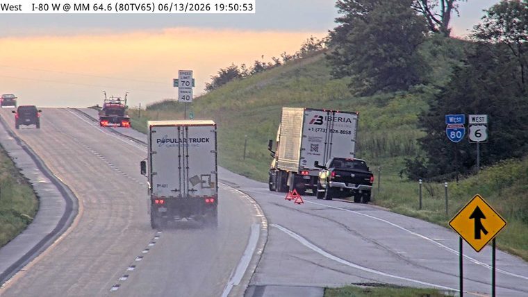 Warning triangles and a pickup truck are on the shoulder near a semi-truck.