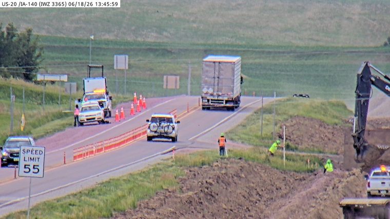 Police car with lights on the shoulder, with cones and workers present