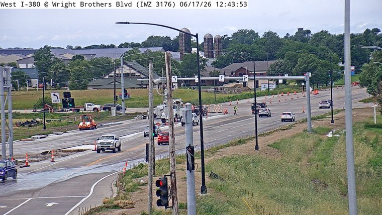 Construction zone with workers and equipment, traffic cones, and a person walking.