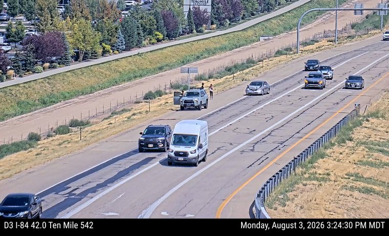 Silver SUV with open driver's door and two people standing nearby on the right shoulder