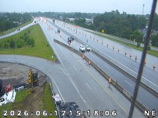 Emergency responders and construction equipment are present on the wet roadway.