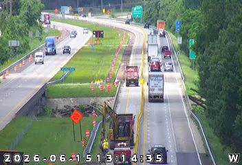 Construction crew and equipment on the highway shoulder, with cones and barriers present.