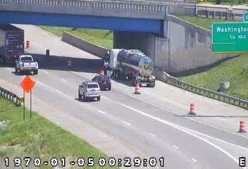 Tanker truck stopped on highway shoulder with traffic cones and what appears to be a responder vehicle.