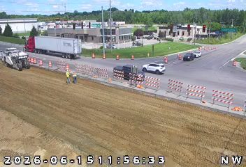 Two workers are present near construction equipment and traffic barriers.