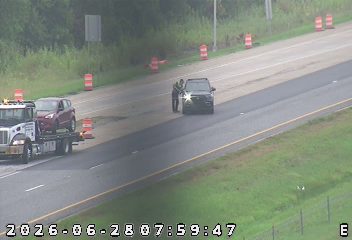 Tow truck with a car on its flatbed and a police vehicle with its lights on near two individuals on the right shoulder