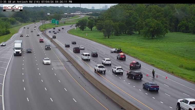 Police car with red and blue lights on the right shoulder, with traffic cones and a person directing traffic.