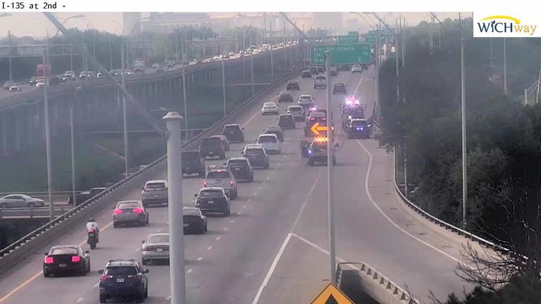 Emergency responders on the highway with flashing lights, causing traffic backup.