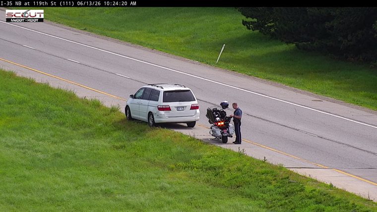 Police officer on motorcycle interacting with a stopped vehicle on the shoulder.
