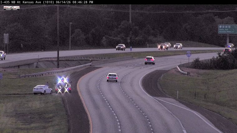 Police car with flashing lights on the shoulder next to a white car.