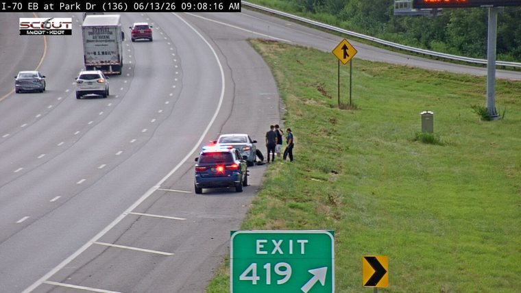 Police car and people on the shoulder near a disabled vehicle.