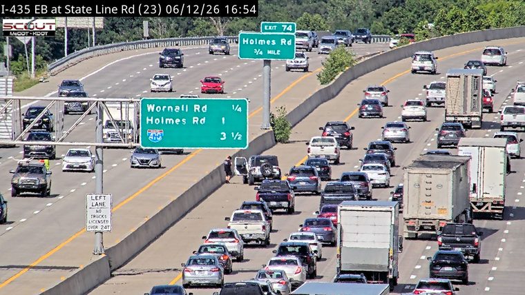 Police officer standing by an open car door on the shoulder of a busy highway.
