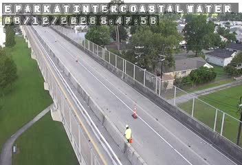 Worker in reflective vest and orange cone on the side of the elevated roadway.