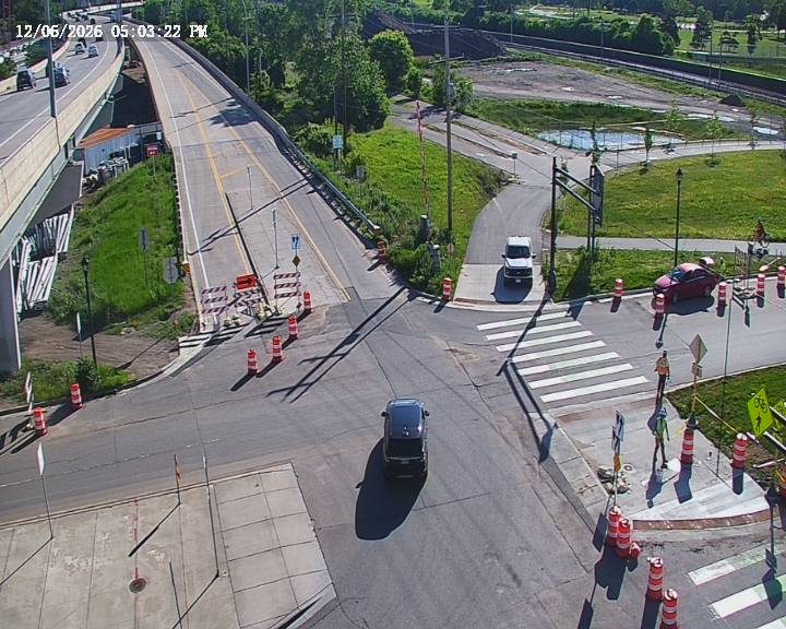 Two construction workers are present near traffic cones and barriers on the roadway.