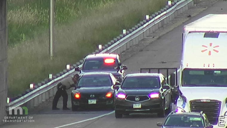 Police car with red lights on the shoulder next to a stopped vehicle