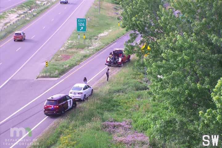 Police car and tow truck on the right shoulder with people standing nearby