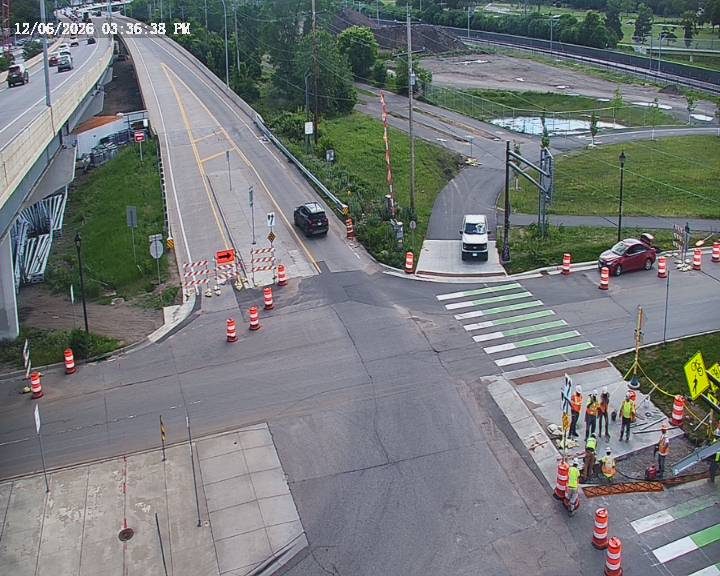 Construction workers are present at a road closure with traffic cones and barriers.