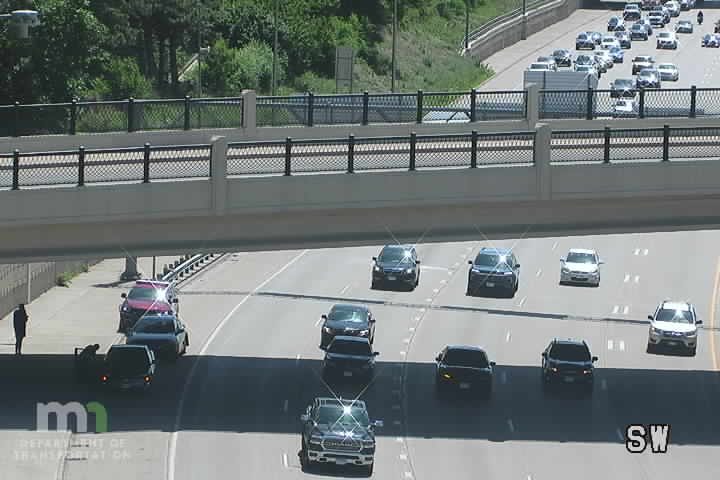Police and other vehicles stopped on the shoulder, with a person standing nearby.