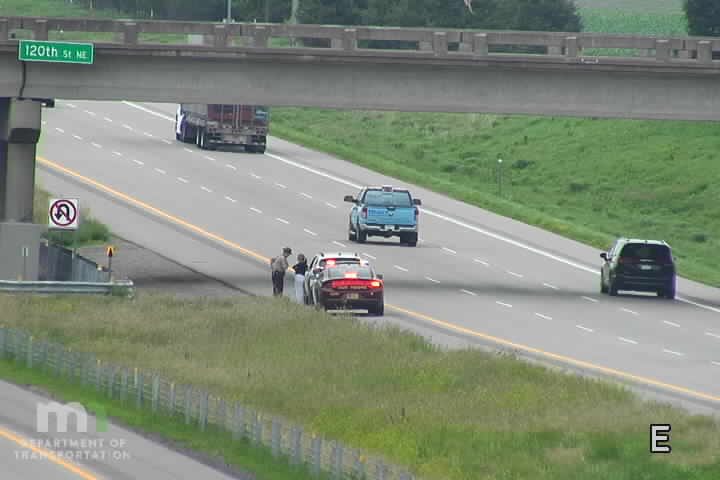 Police car with two individuals standing next to it on the right shoulder