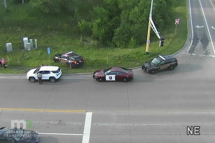 Two sheriff vehicles and a civilian vehicle stopped in the roadway, with a person standing near the white vehicle.