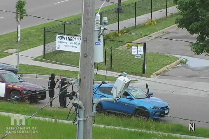 State trooper and another person stand by a blue car with its hood open.